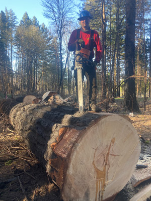 crew member standing on log with saw